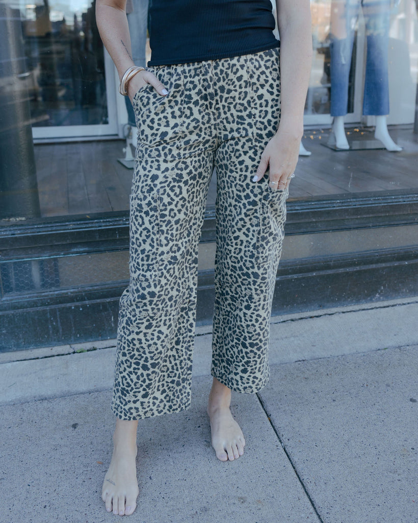 Person wearing leopard print pants standing on a sidewalk.