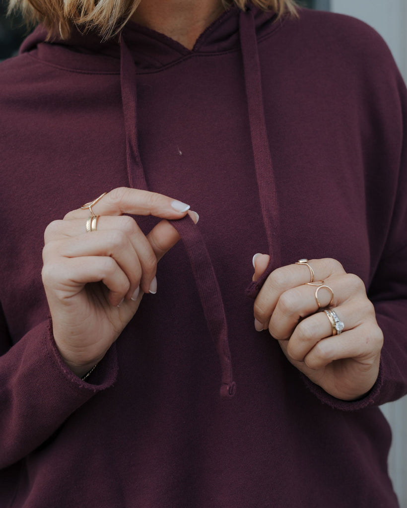 Person wearing a maroon hoodie with hands adjusting the hood against a neutral background