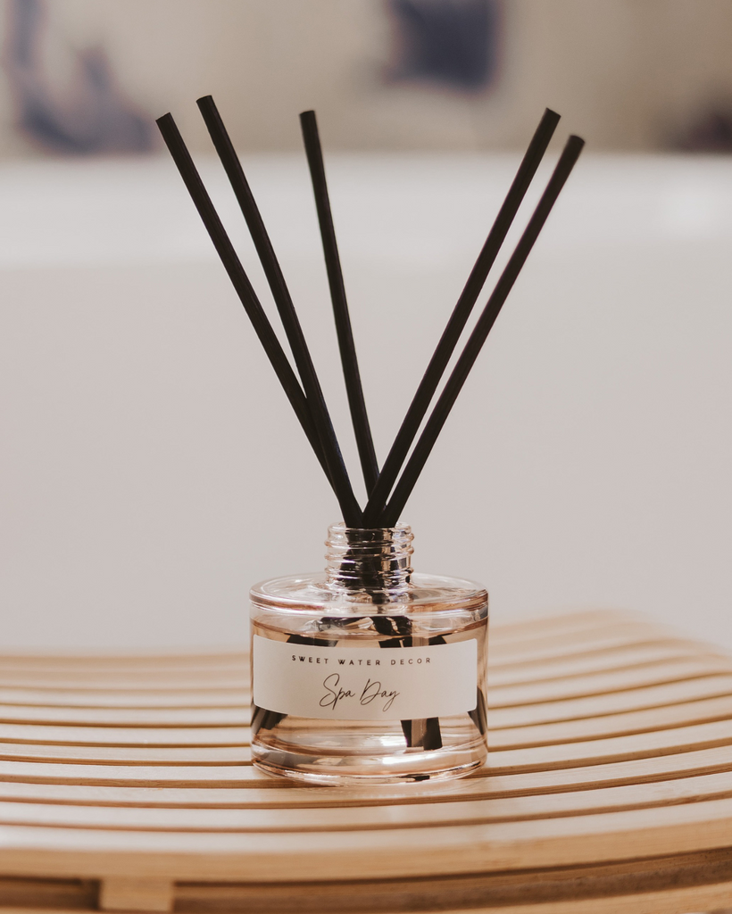 Reed diffuser with black sticks in a clear bottle on a wooden surface