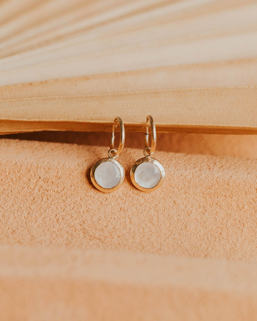 Pair of gold earrings with round stones on a beige fabric background