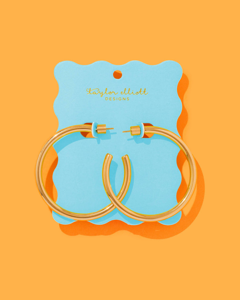 Gold hoop earrings on a blue card with 'Sophie Allport' branding against an orange background