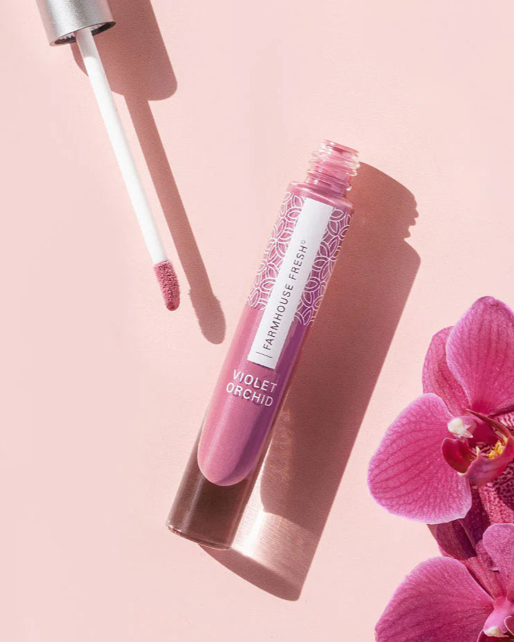 Lip gloss with applicator and pink orchid on a light pink background