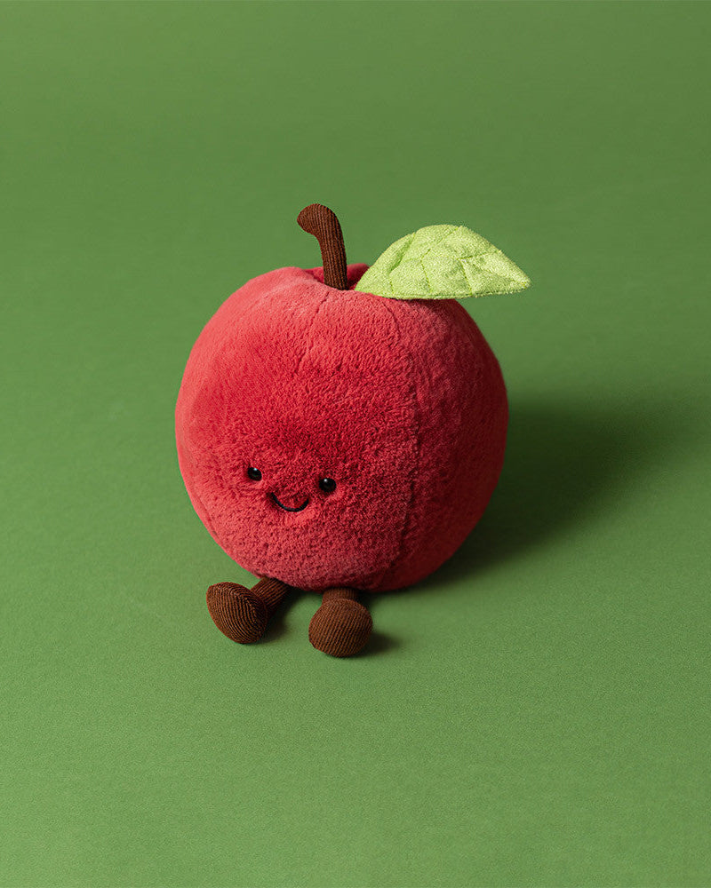 Plush toy shaped like a red apple with a green leaf on a green background
