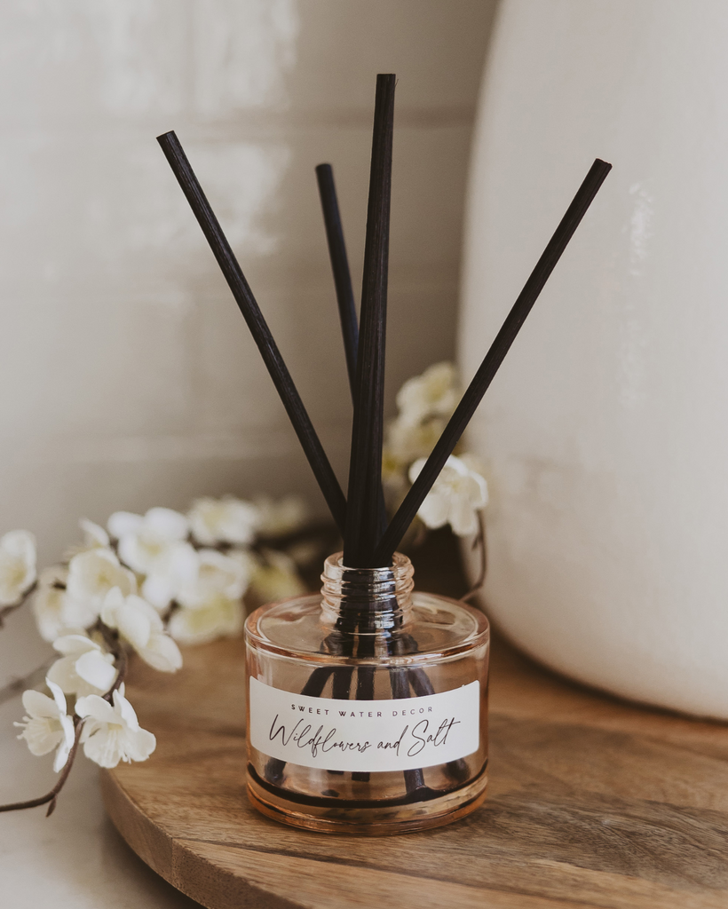 Diffuser with black sticks on a wooden surface with white flowers in the background