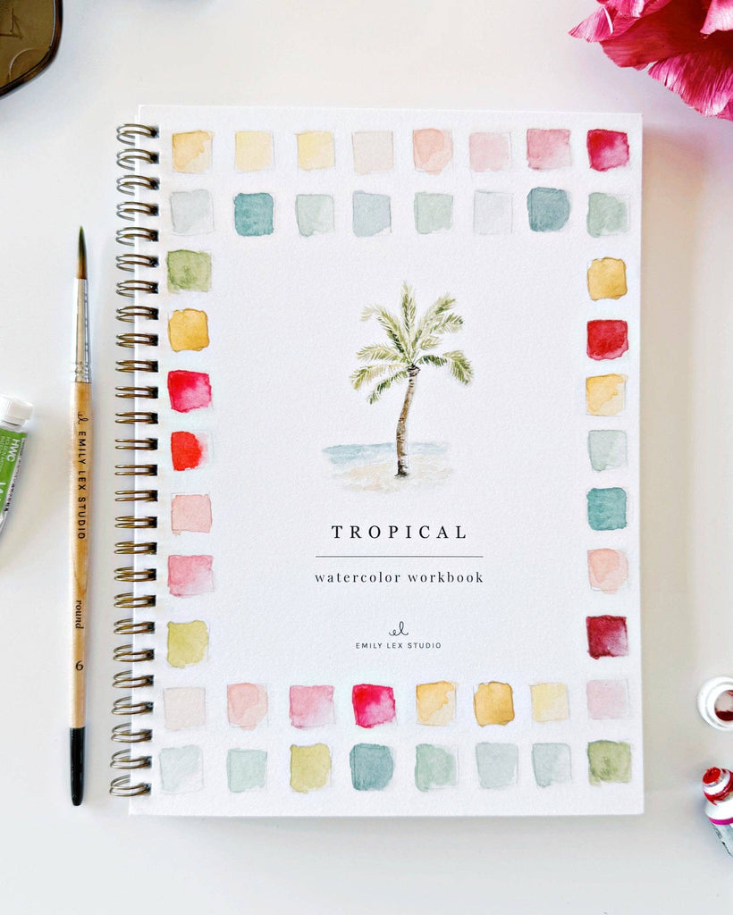 Tropical watercolor workbook with a paintbrush and paint tube on a white surface