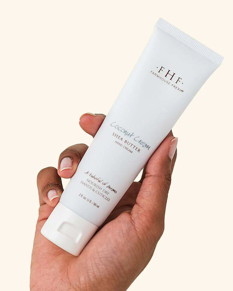 Hand holding a tube of FHF Coconut Dream body butter against a white background