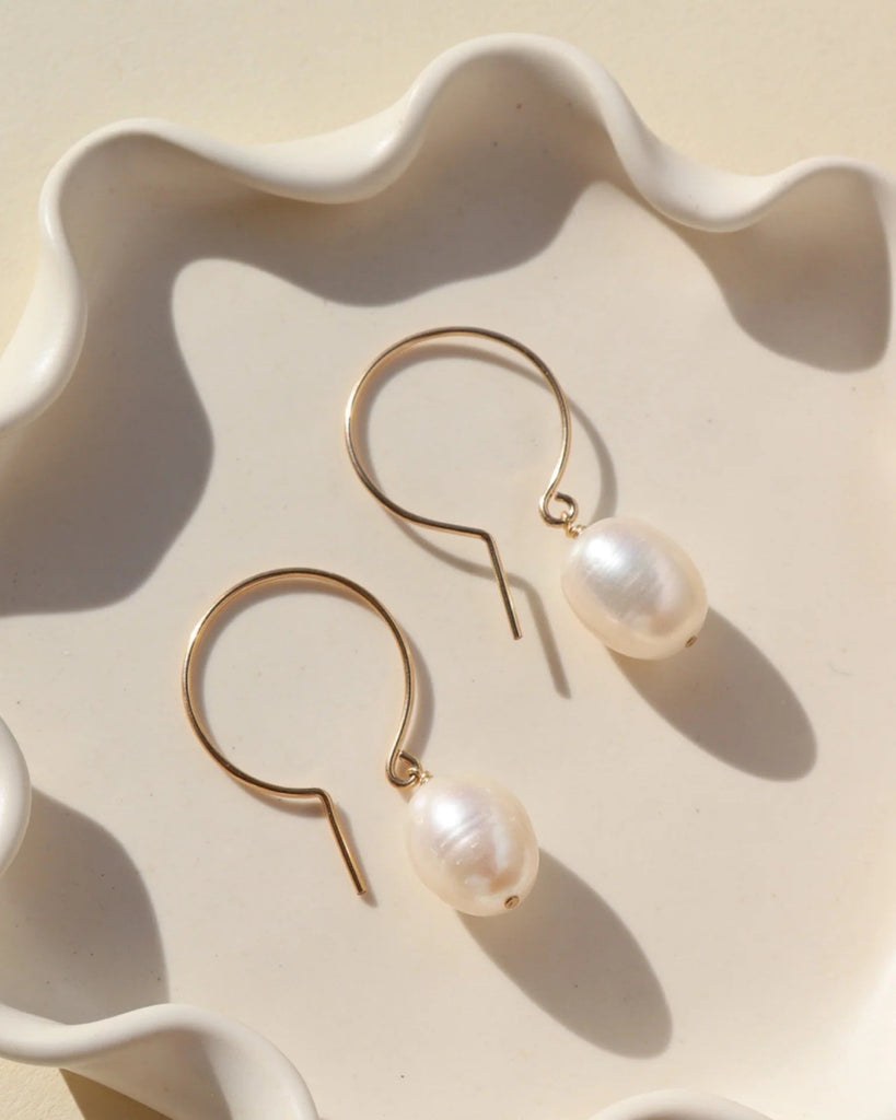 Gold earrings with pearls on a decorative white dish