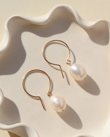 Gold earrings with pearls on a decorative white dish