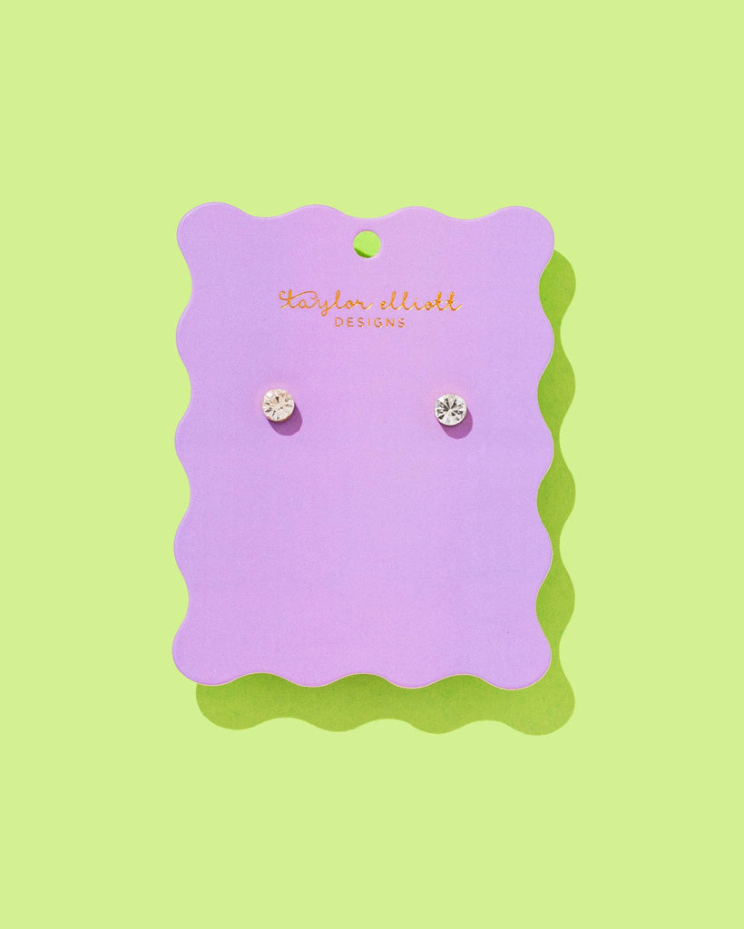 Pair of earrings on a purple card with 'Taylor Elliott' branding against a green background