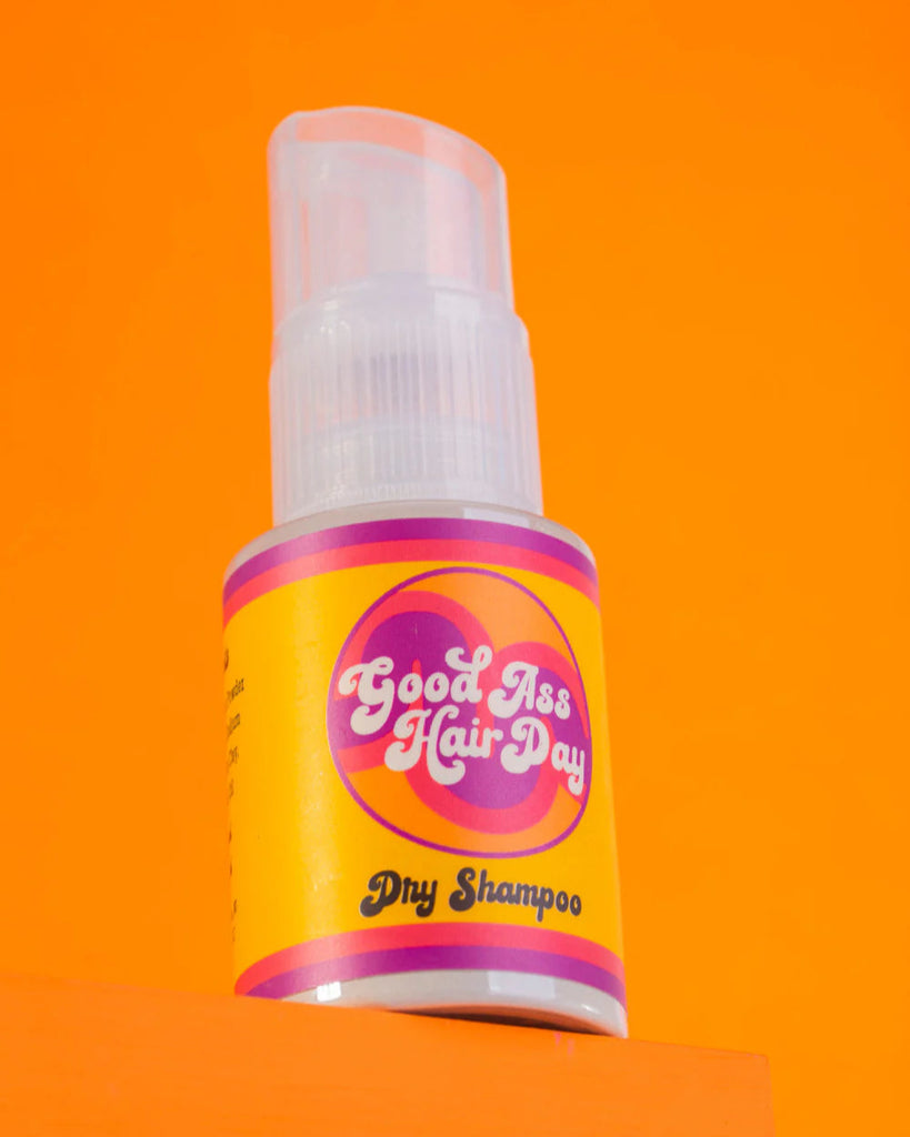 Bottle of 'Good Ass Hair Day' dry shampoo on an orange background