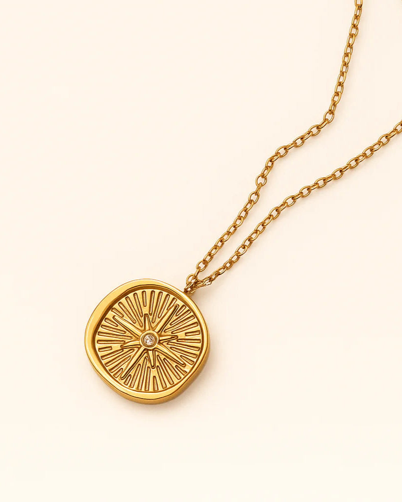 Gold necklace with a round pendant on a light beige background