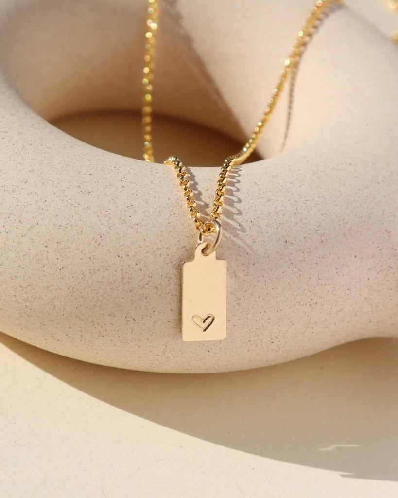 Gold necklace with a heart pendant on a beige surface