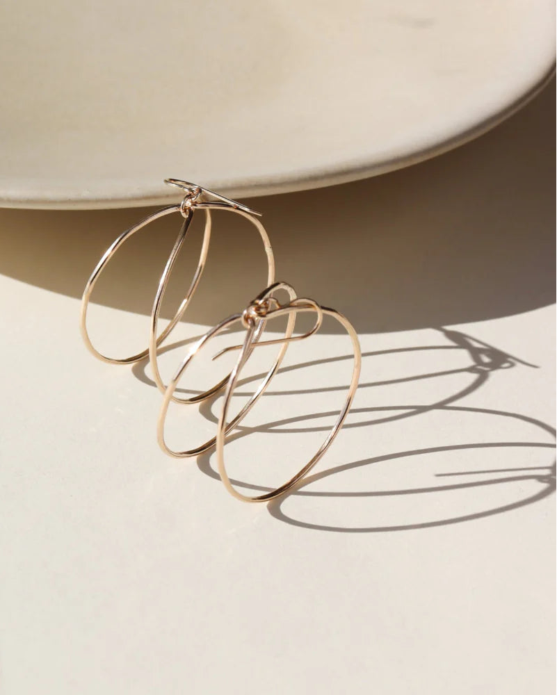 Gold hoop earrings on a beige surface with a soft focus background