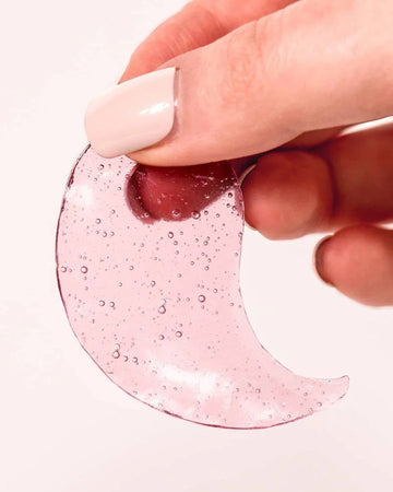 Hand holding a pink crescent-shaped object with bubbles on a white background