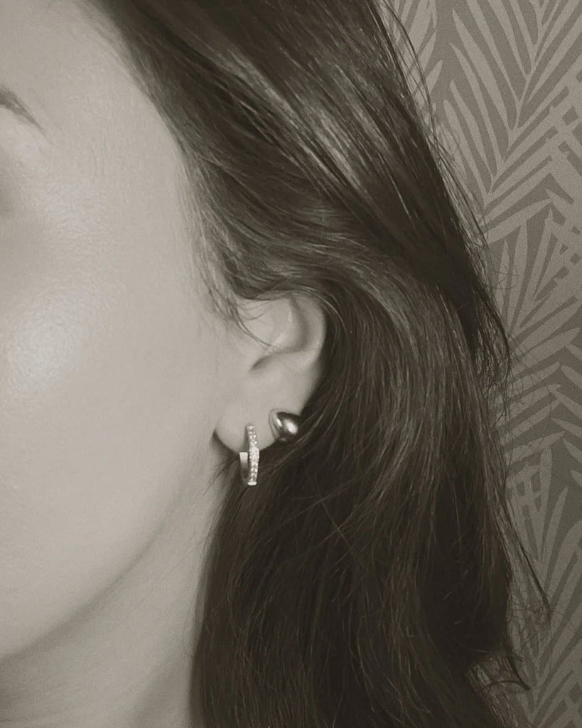 Close-up of a woman's ear with earrings against a patterned wall.