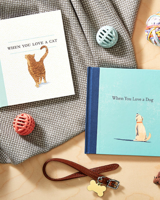 Two books titled 'When You Love a Cat' and 'When You Love a Dog' on a textured surface with pet-related items.
