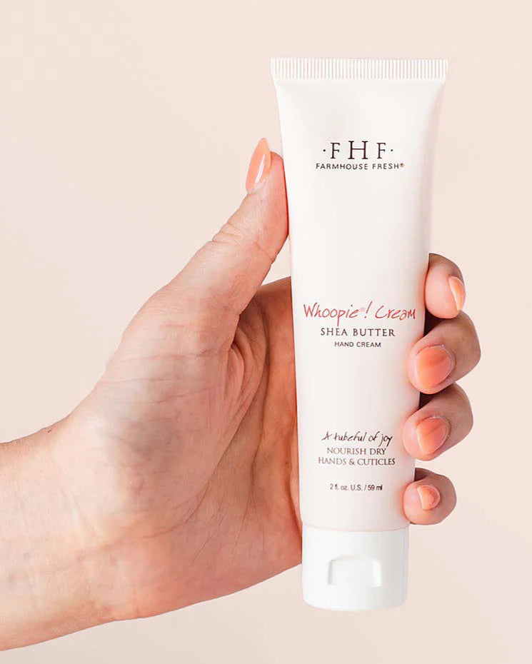 Hand holding a tube of Farmhouse Fresh Whipped Cream Shea Butter hand cream against a beige background